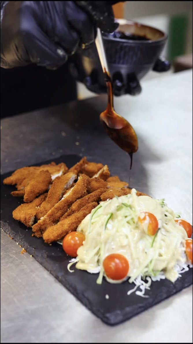 Sauce being spooned over chicken katsu on slate