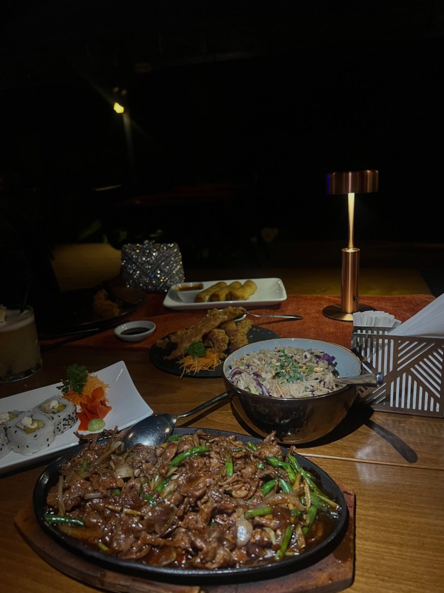Sizzling beef on a cast iron plate with spring rolls behind